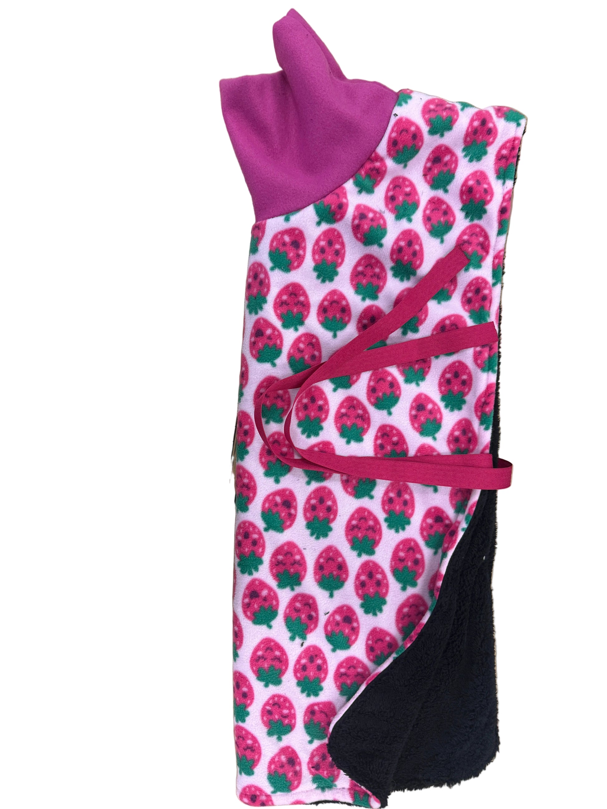 A folded dog fleece blanket with a pink and green strawberry pattern, a purple collar, and a magenta tie strap, laid on top of a cardboard display stand.
